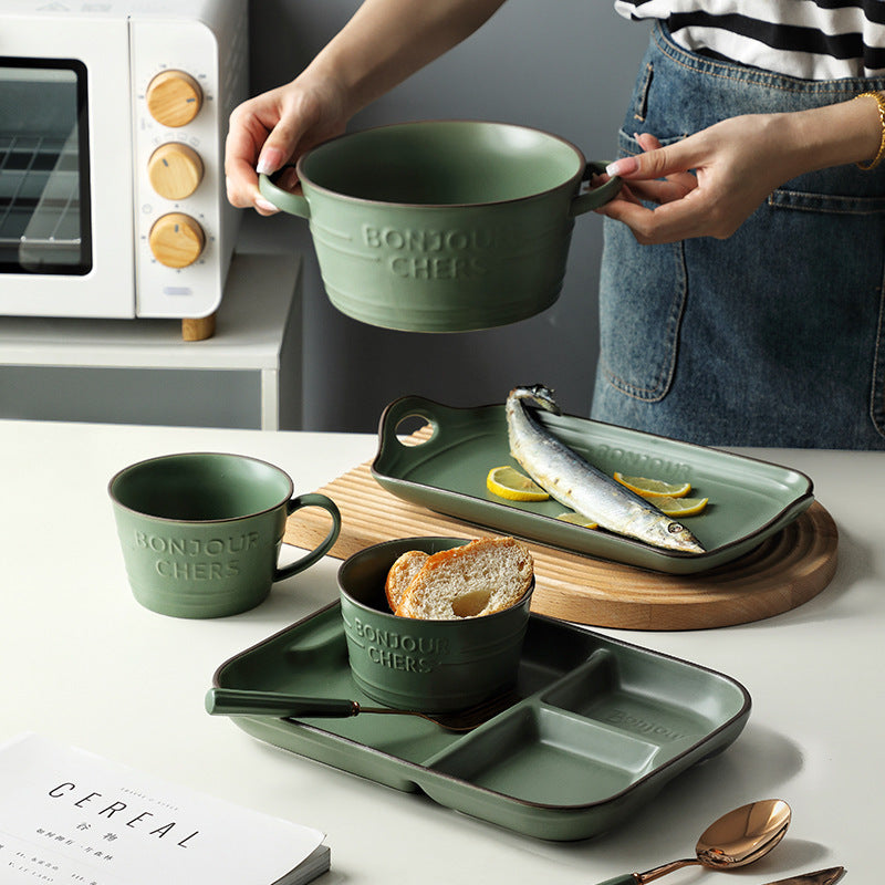 Scandinavian style ceramic tableware, including green breakfast cup, rice bowl, rectangular plate, and fork, showcased in kitchen setting.