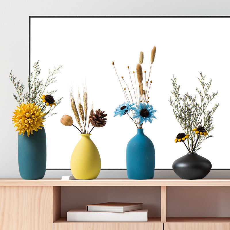 Handmade ceramic vases in dark green, yellow, blue, and black colors displayed on a shelf with flowers, modern and simple style.