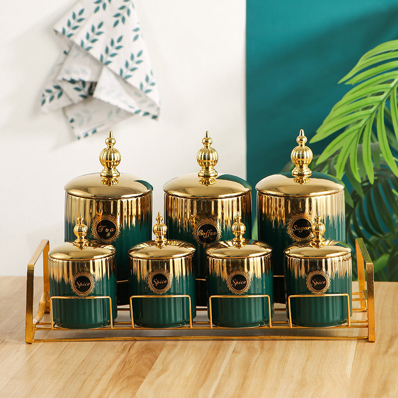 Round ceramic storage jars with gold lids in dark green on a wooden shelf.