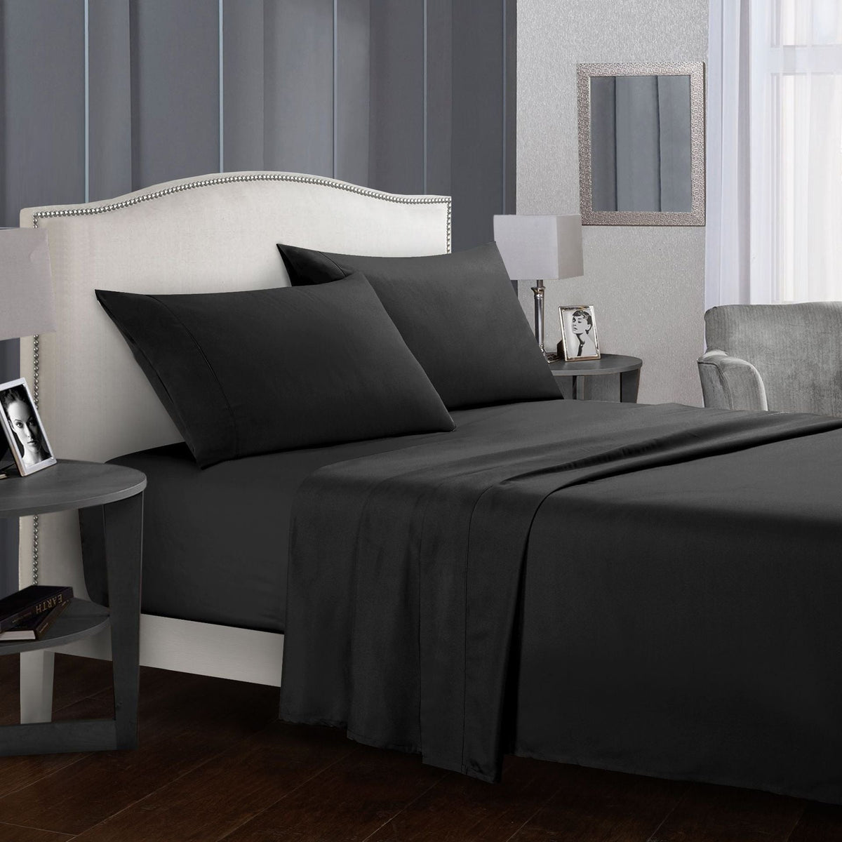 Dark gray four-piece bed sheet set on bed with pillows and stylish decor.