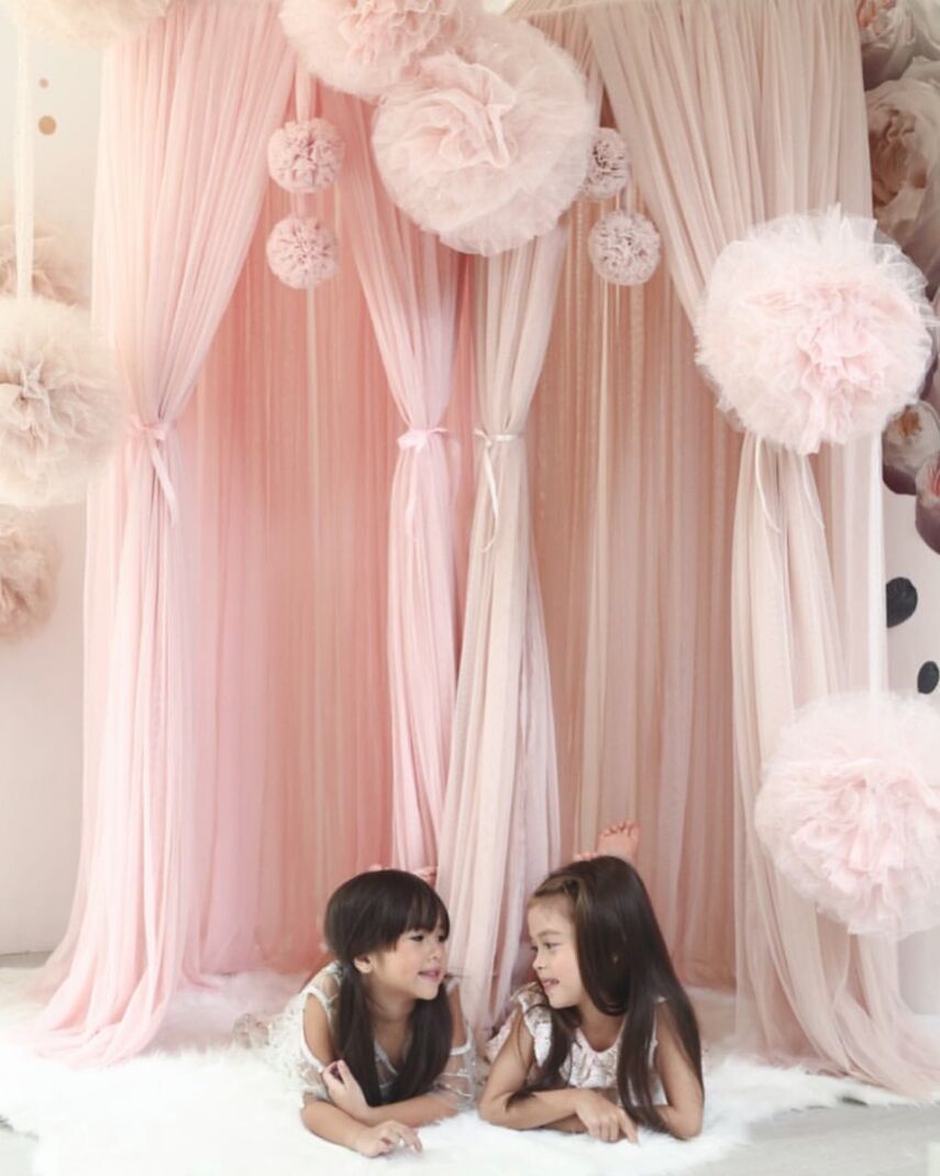 Children's room with pink yarn large ball ornaments hanging near draped curtains.