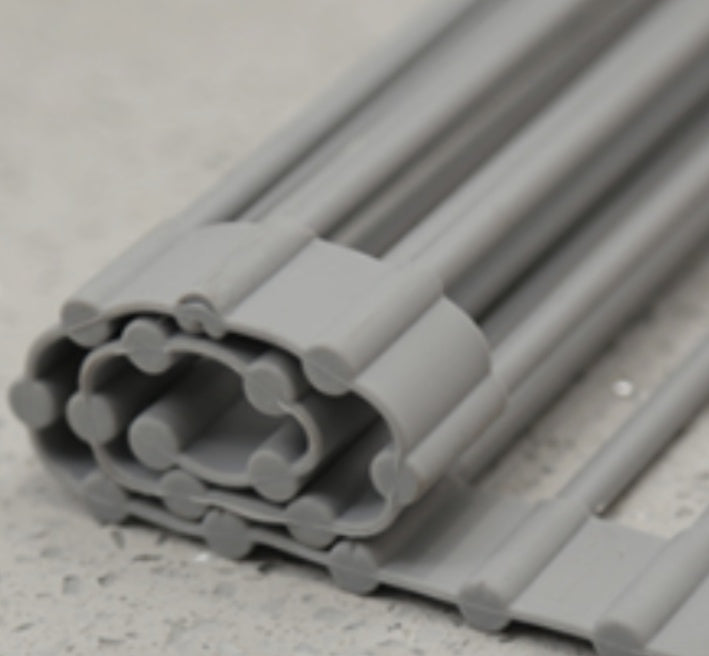 Folding kitchen drain sink rack in stainless steel, rolled for storage on countertop.