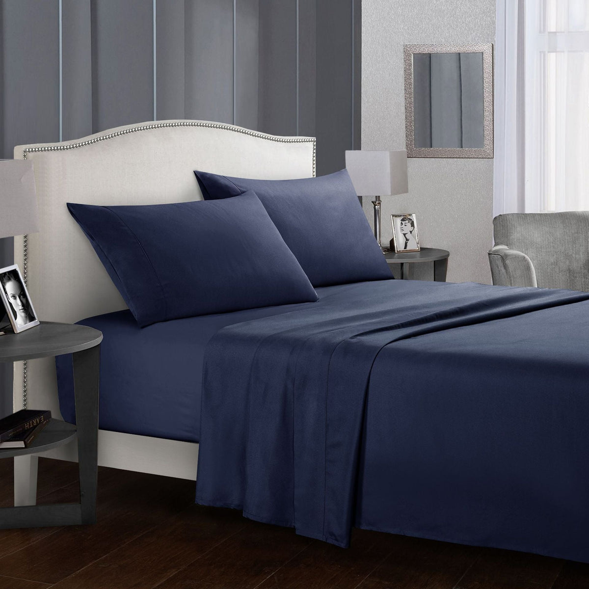 Navy blue four-piece bed sheet set on a white bed in a modern bedroom.