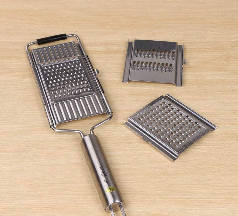 Stainless steel grater with interchangeable blades on a wooden surface.